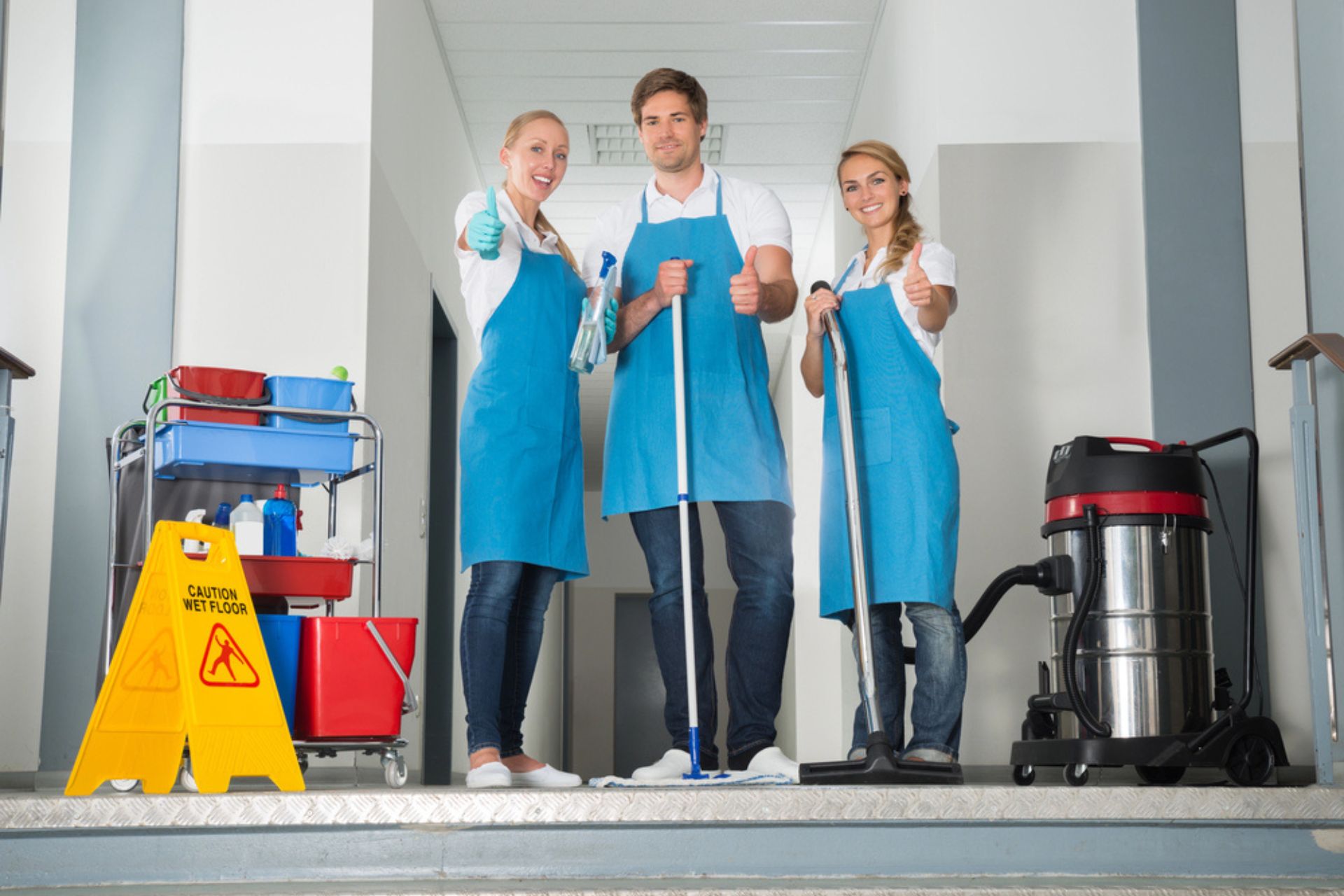 Équipe de nettoyage professionnelle en uniforme bleu, équipée de matériel de nettoyage, aspirateur industriel et chariot de produits, prête à entretenir des espaces professionnels.